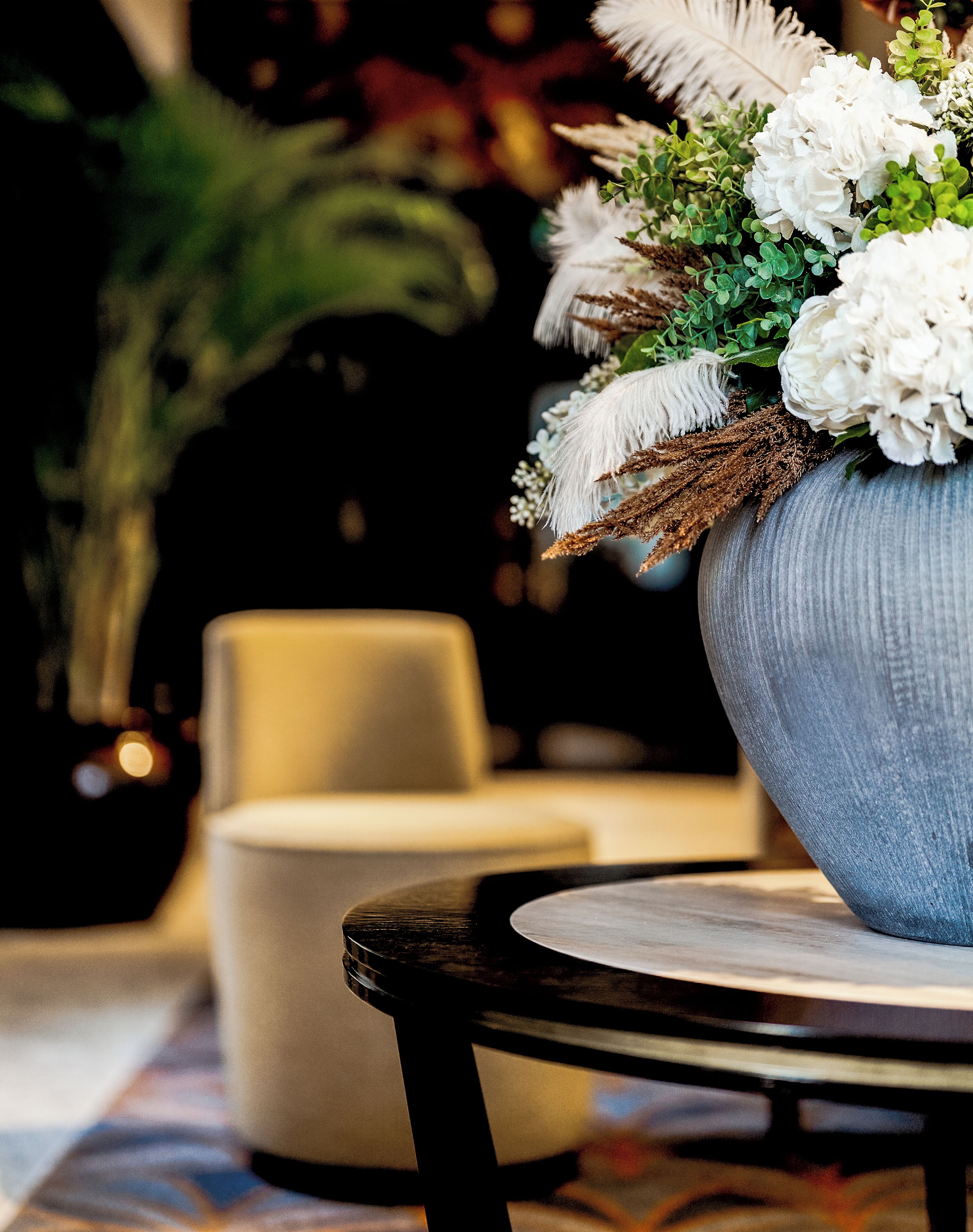 A round table with a vase of white flowers and greenery.