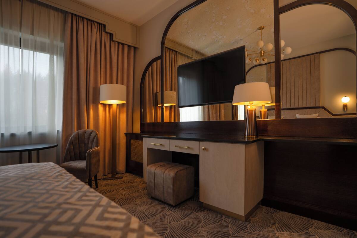 A hotel room with a bed, a desk with a chair, a television, and a large mirror.