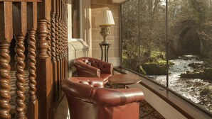 A room with a large window overlooking a river, a leather armchair, a lamp, and wooden furniture. - Crossbasket Castle Hotel & Restaurant (Glasgow)