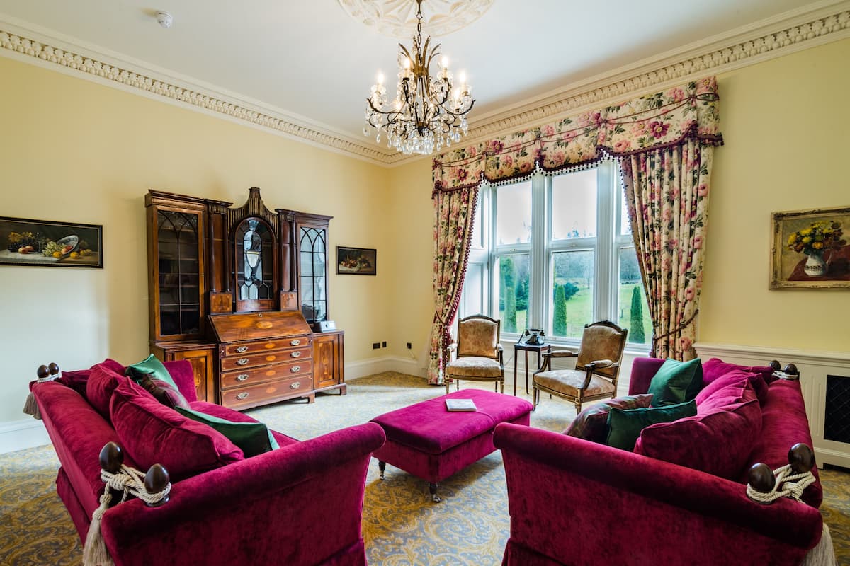 A room with a large window, a chandelier, a wooden cabinet, and two red velvet sofas.