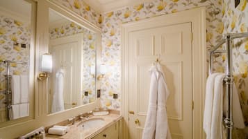Un baño con lavamanos, espejo y puerta blancos, con papel tapiz floral y toallas blancas.