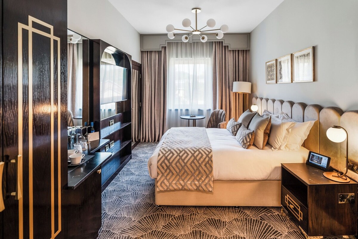 Una habitación de hotel con una cama grande, un televisor, un escritorio con lámpara y una silla.