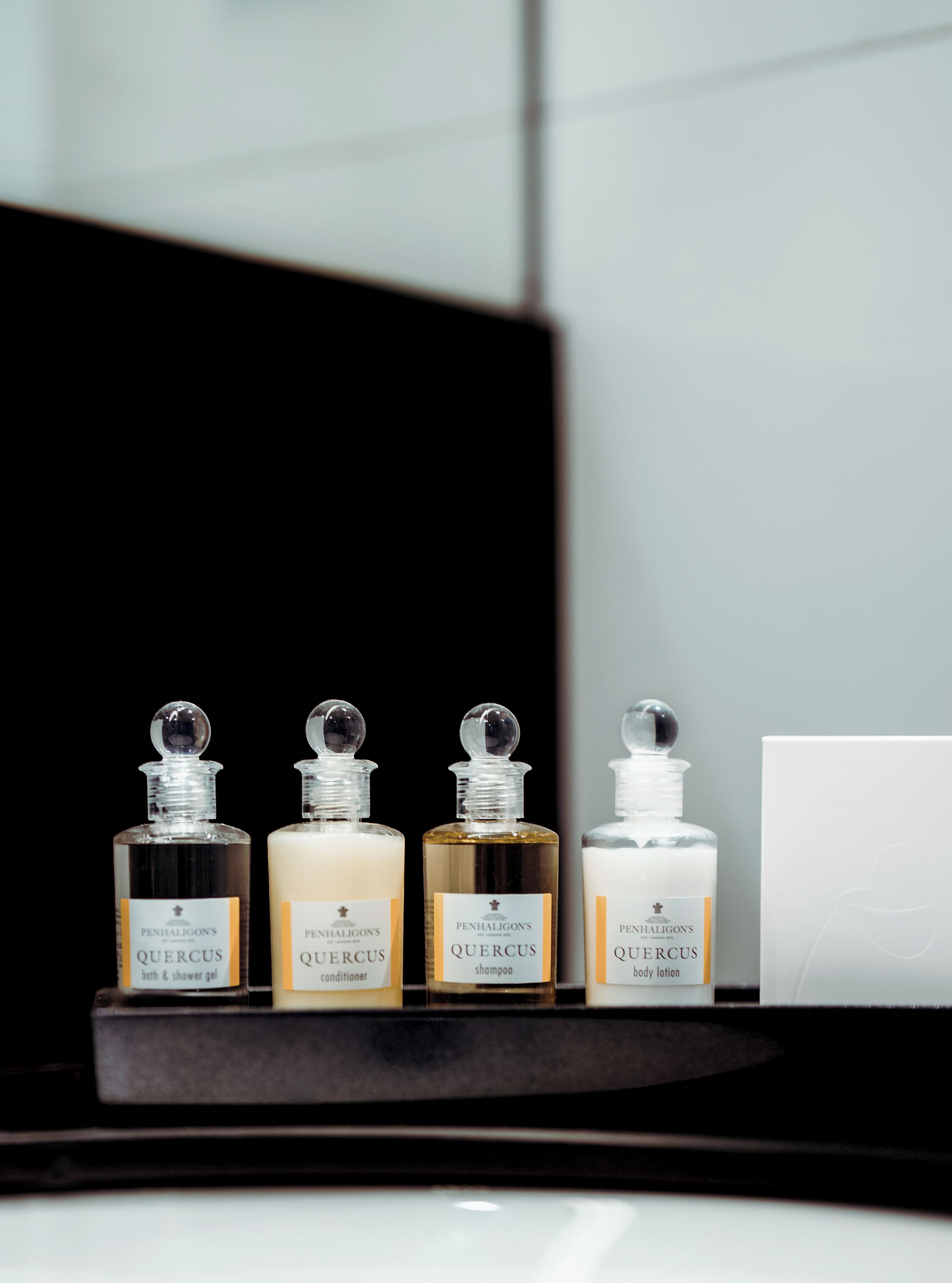 Cuatro botellas de productos de baño Penhaligon's Quercus sobre una estantería.