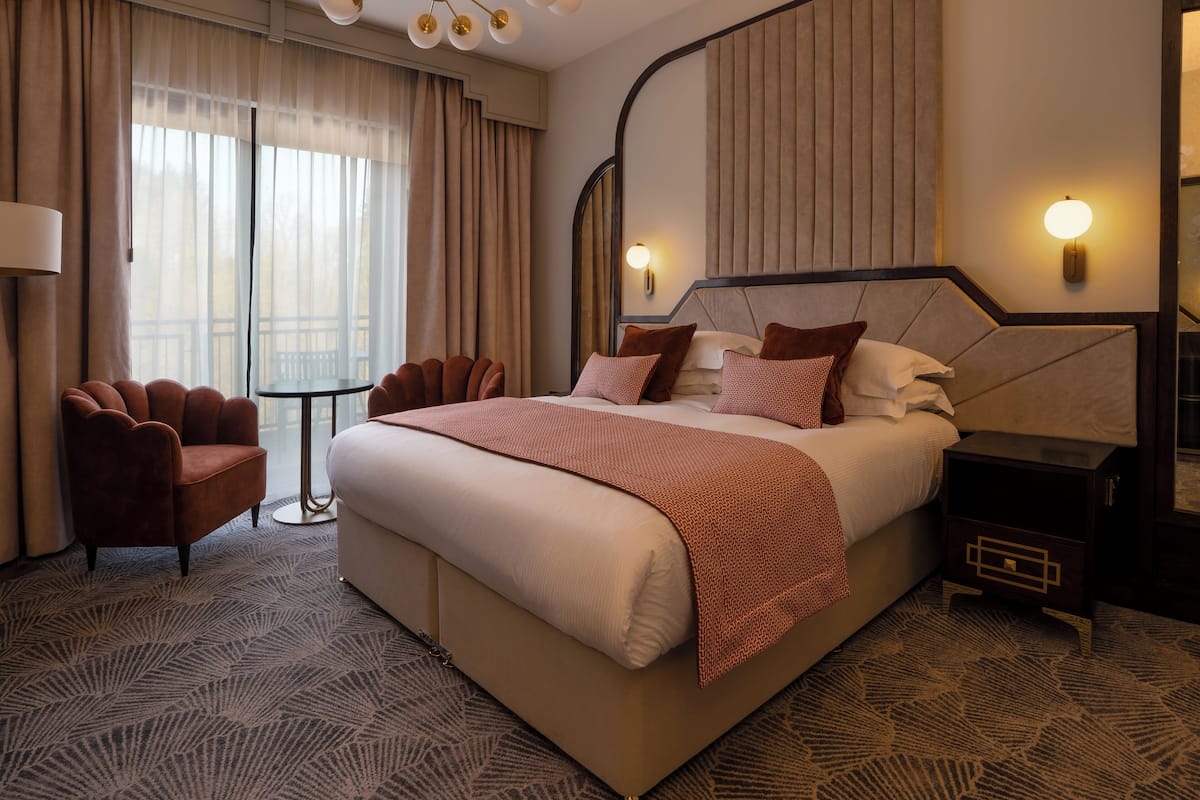 A hotel room with a large bed, a chair, a bedside table, and a lamp.