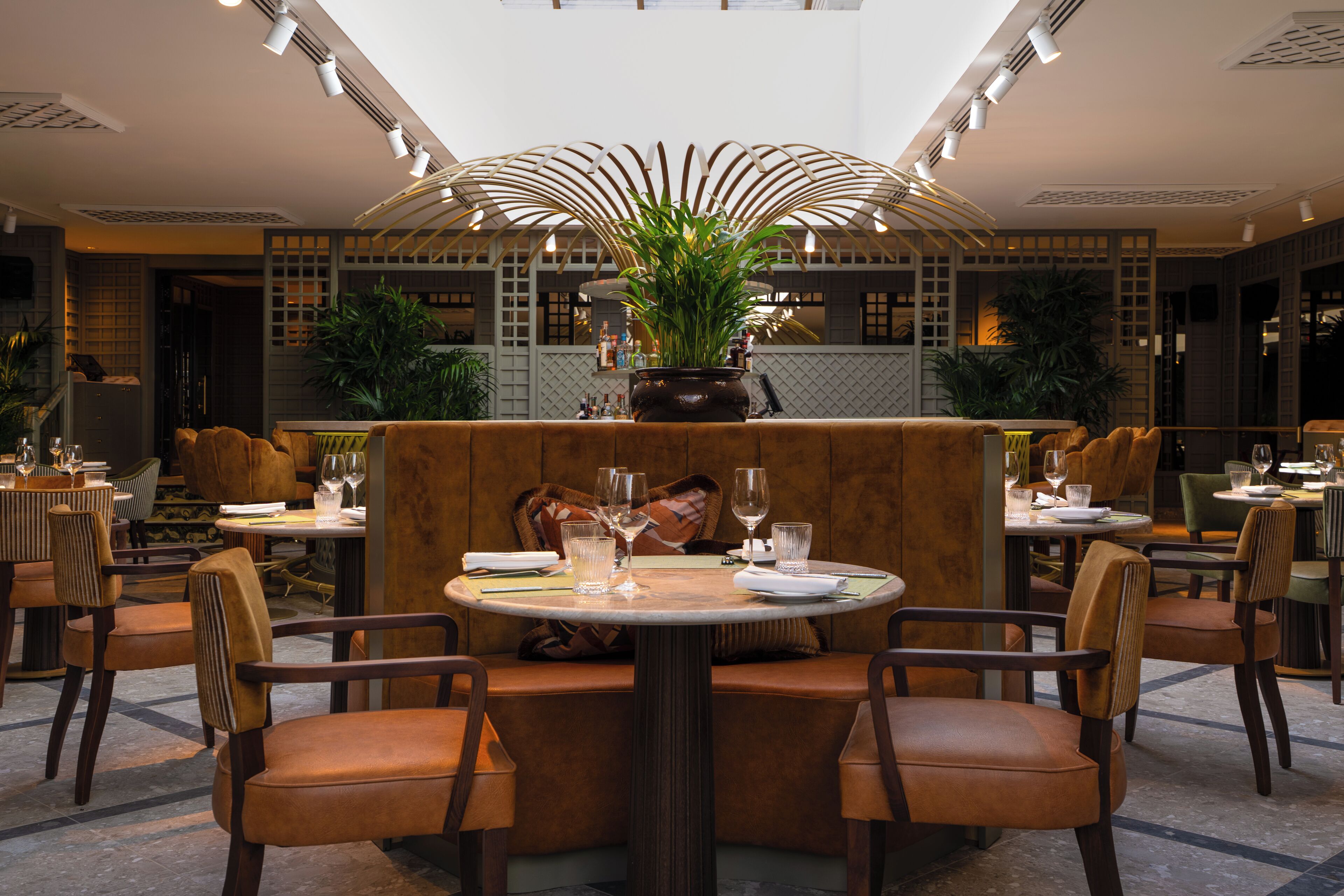 A restaurant with round tables, brown upholstered booths, and potted plants.