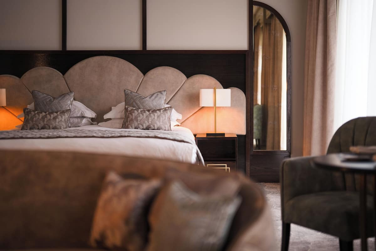 A modern hotel room with a large bed, a nightstand with a lamp, and a chair.