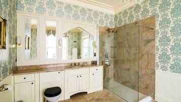 A bathroom with a large mirror, white cabinetry, a toilet, a shower with glass doors, and patterned wallpaper.