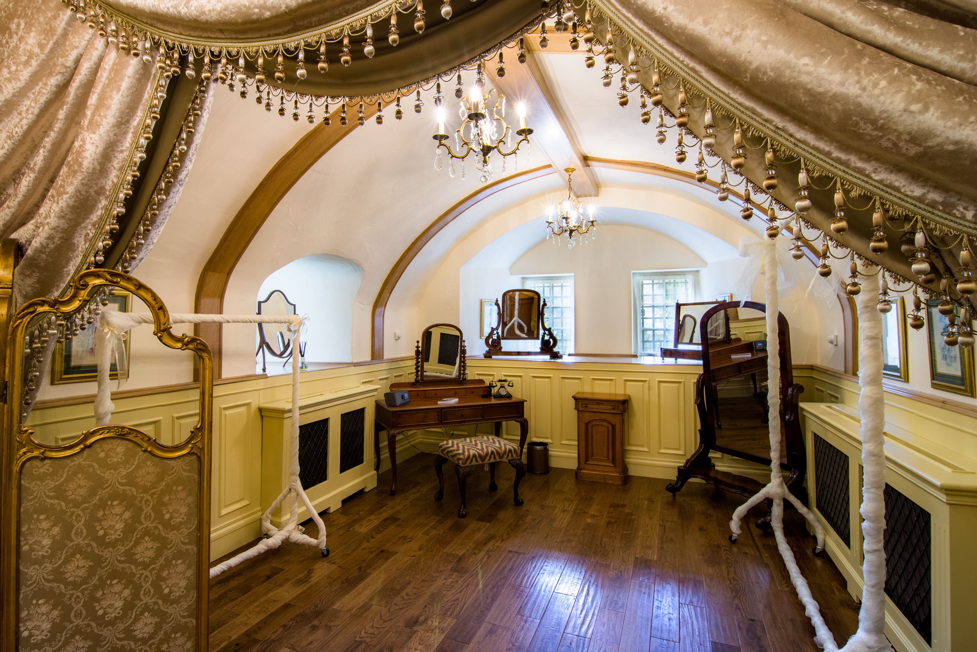 Une pièce dotée d’un plafond voûté, de lustres, d’un bureau en bois, d’une chaise et d’un grand miroir.