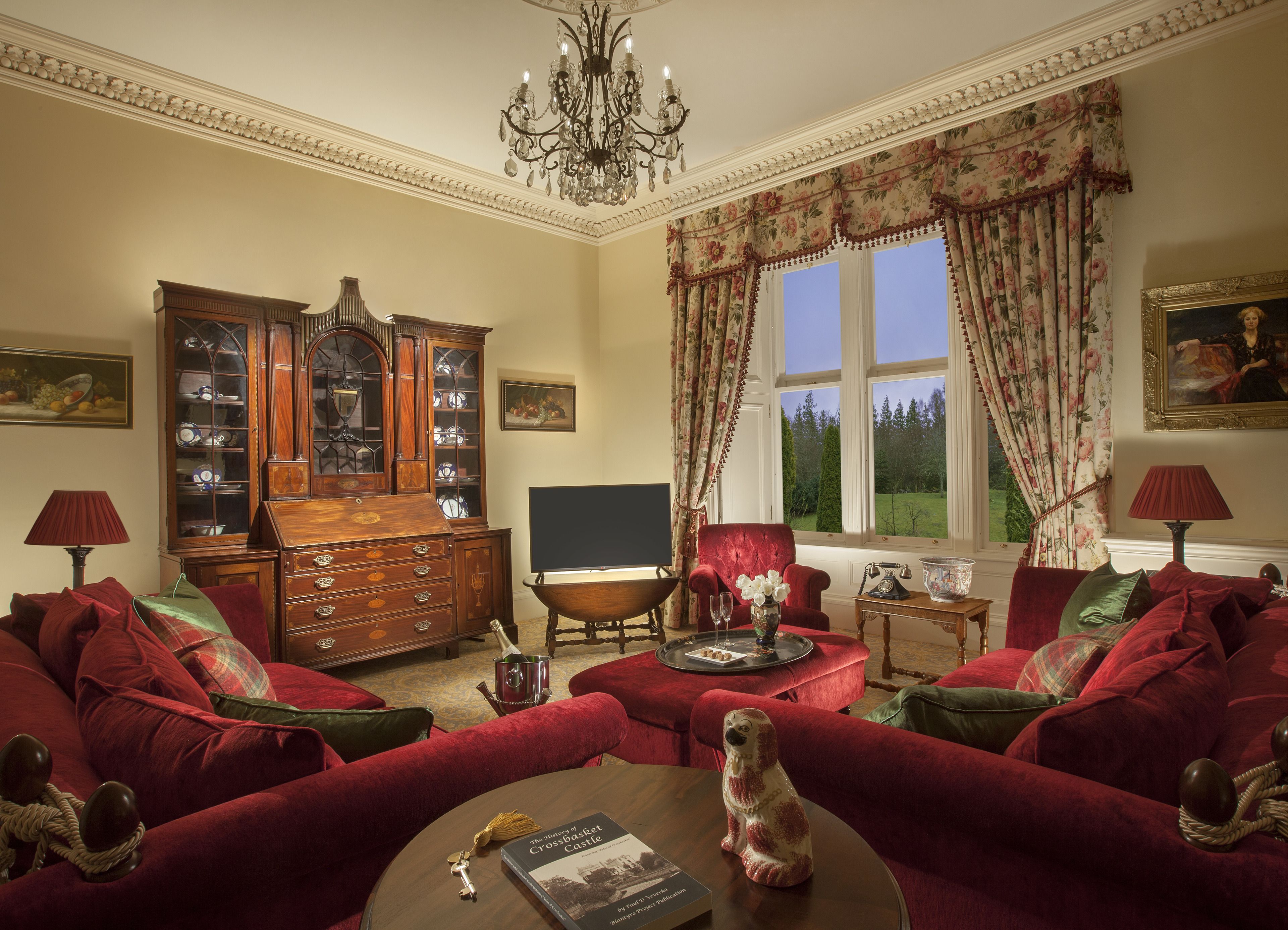Une pièce de style traditionnel, avec une grande armoire en bois, un fauteuil rouge, un canapé, une cheminée et une vue sur une forêt par la fenêtre.