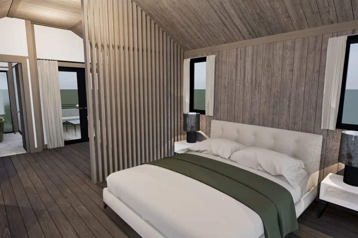A bedroom with a large bed, a nightstand, a window, and a wooden ceiling.