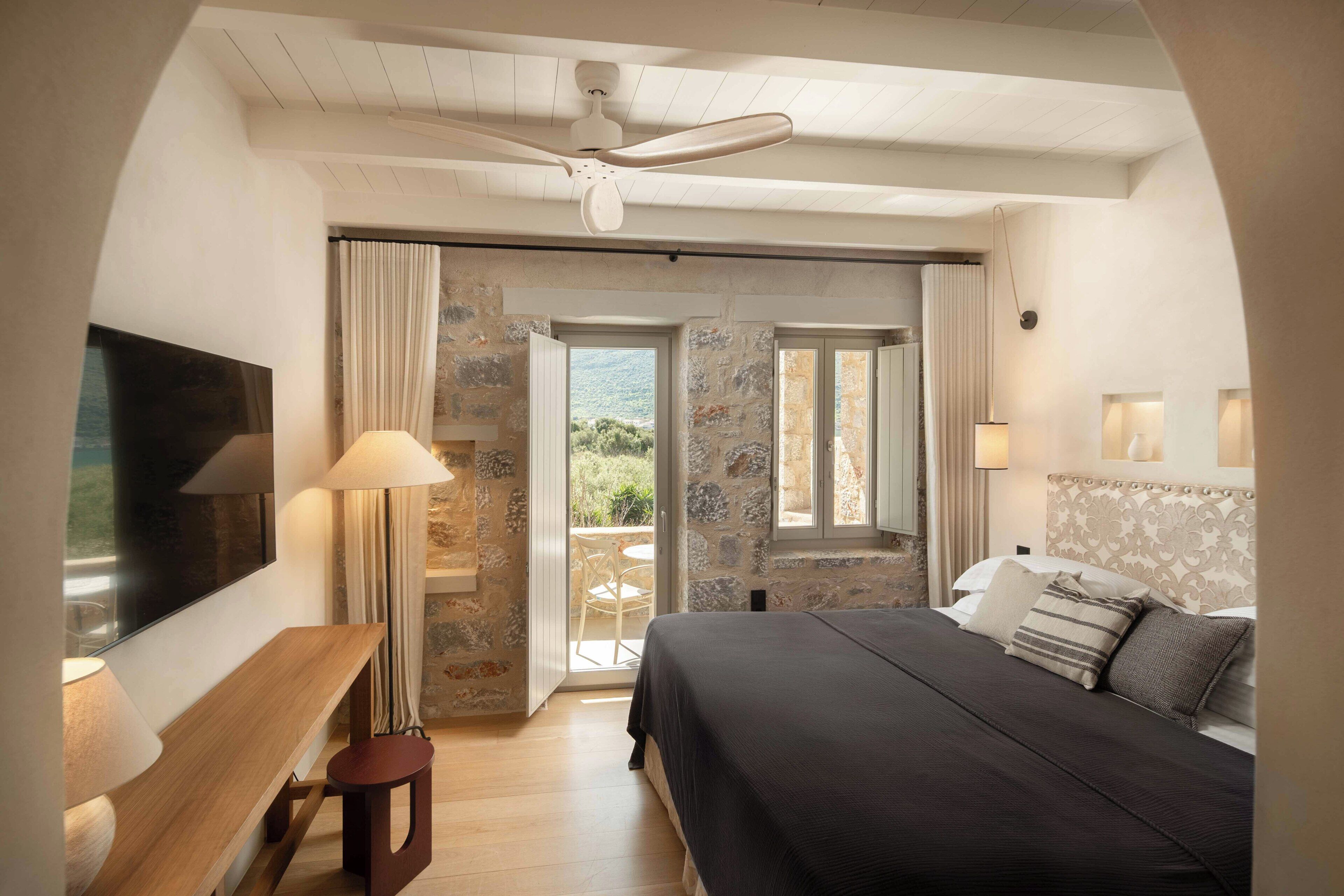 Un dormitorio con cama, escritorio, silla, ventilador de techo y vista al exterior.