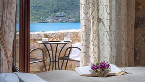 Une pièce avec un balcon donnant sur la côte, une table avec un livre et des fleurs, et une vue sur un bâtiment situé sur une colline.