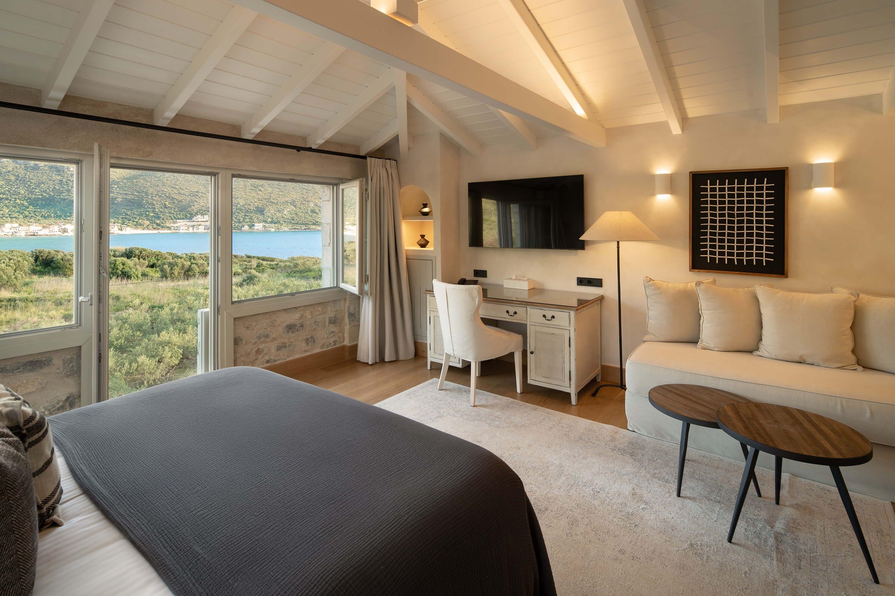 Ein Schlafzimmer mit einem großen Bett, einem Schreibtisch, einer Couch und Blick auf einen See.