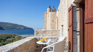 Un bâtiment en pierre doté d’un balcon donnant sur la mer, une table où est servi le petit-déjeuner et une vue sur la côte.