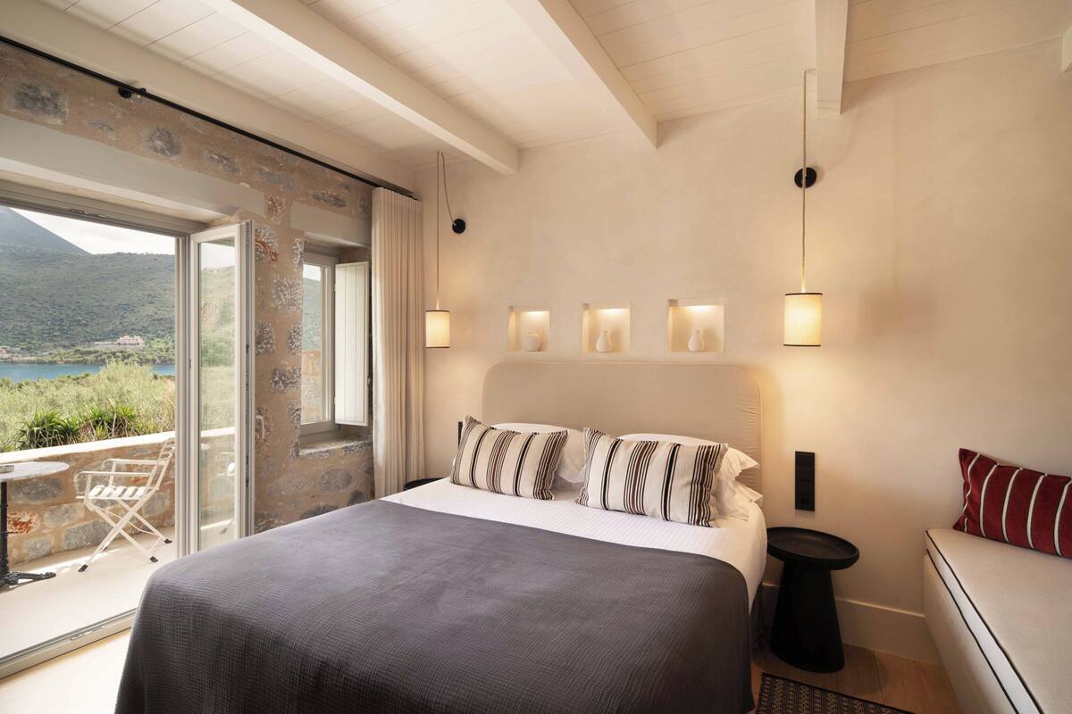 Een slaapkamer met een groot bed, uitzicht door een glazen deur, een kleine tafel en een bank.