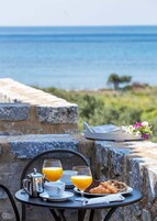 A table with breakfast items, a view of the sea, and a stone wall.