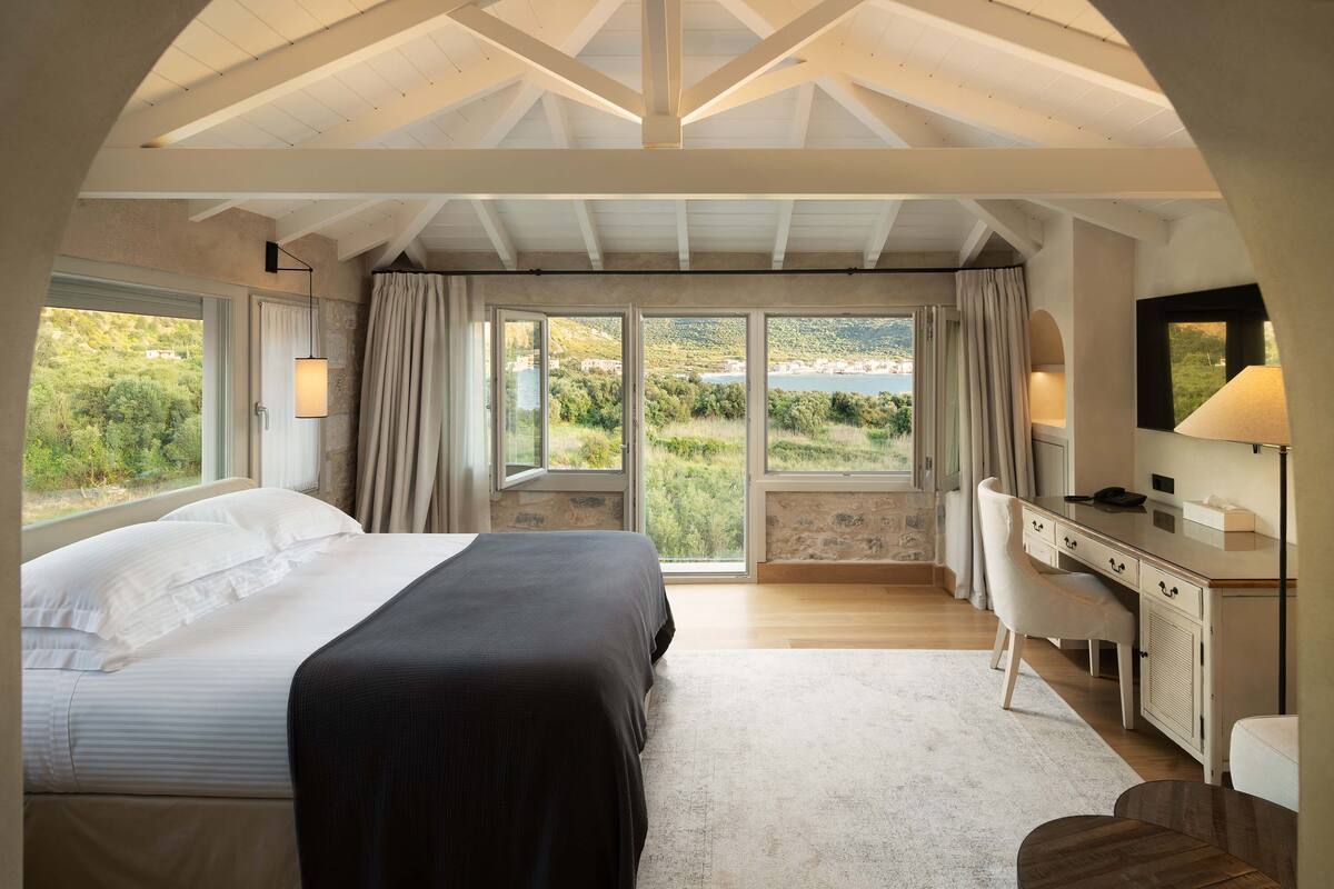 Een slaapkamer met een bed, bureau en grote ramen met uitzicht op een mooi landschap.