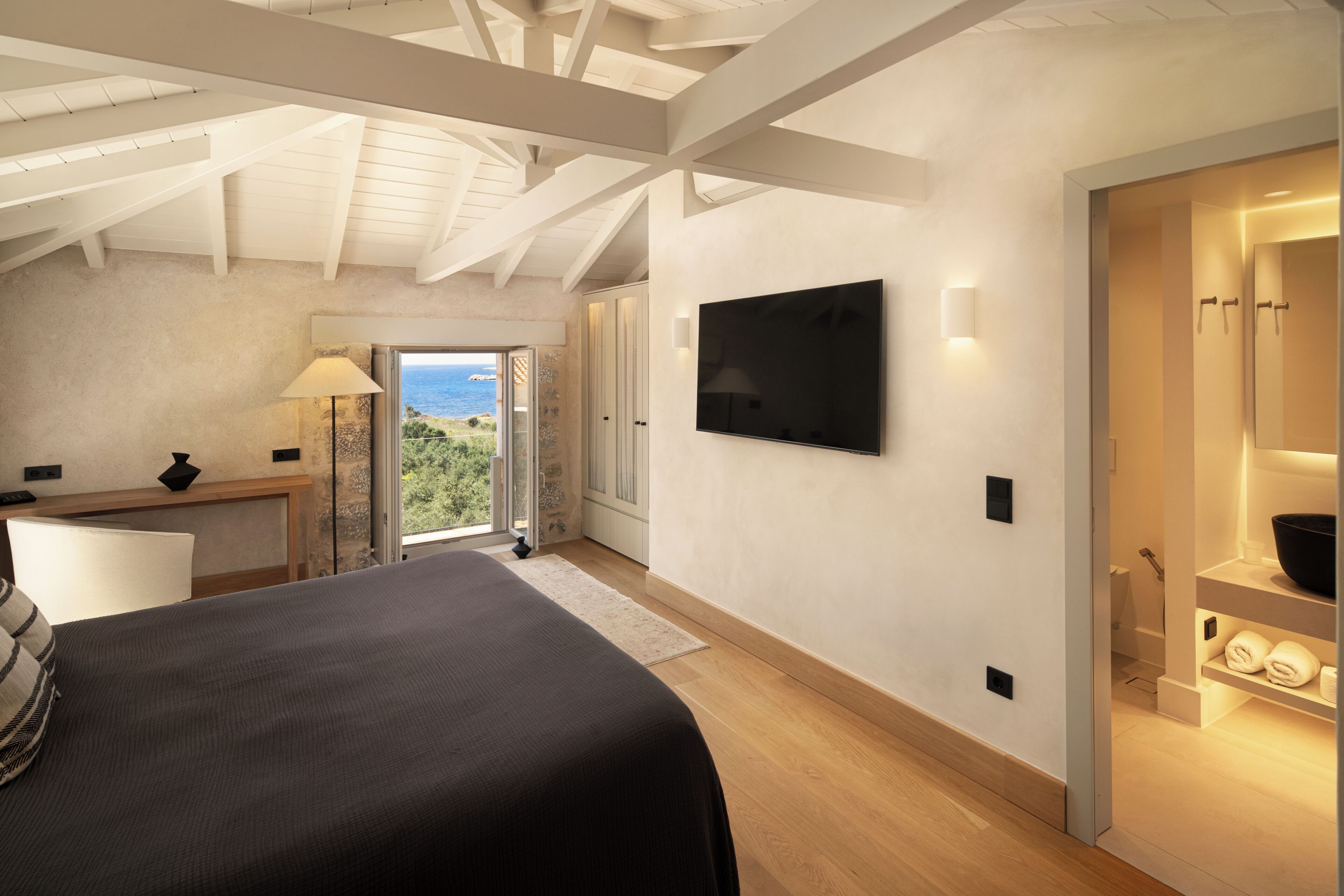 A bedroom with a bed, a TV, a desk, and a view of the outdoors.