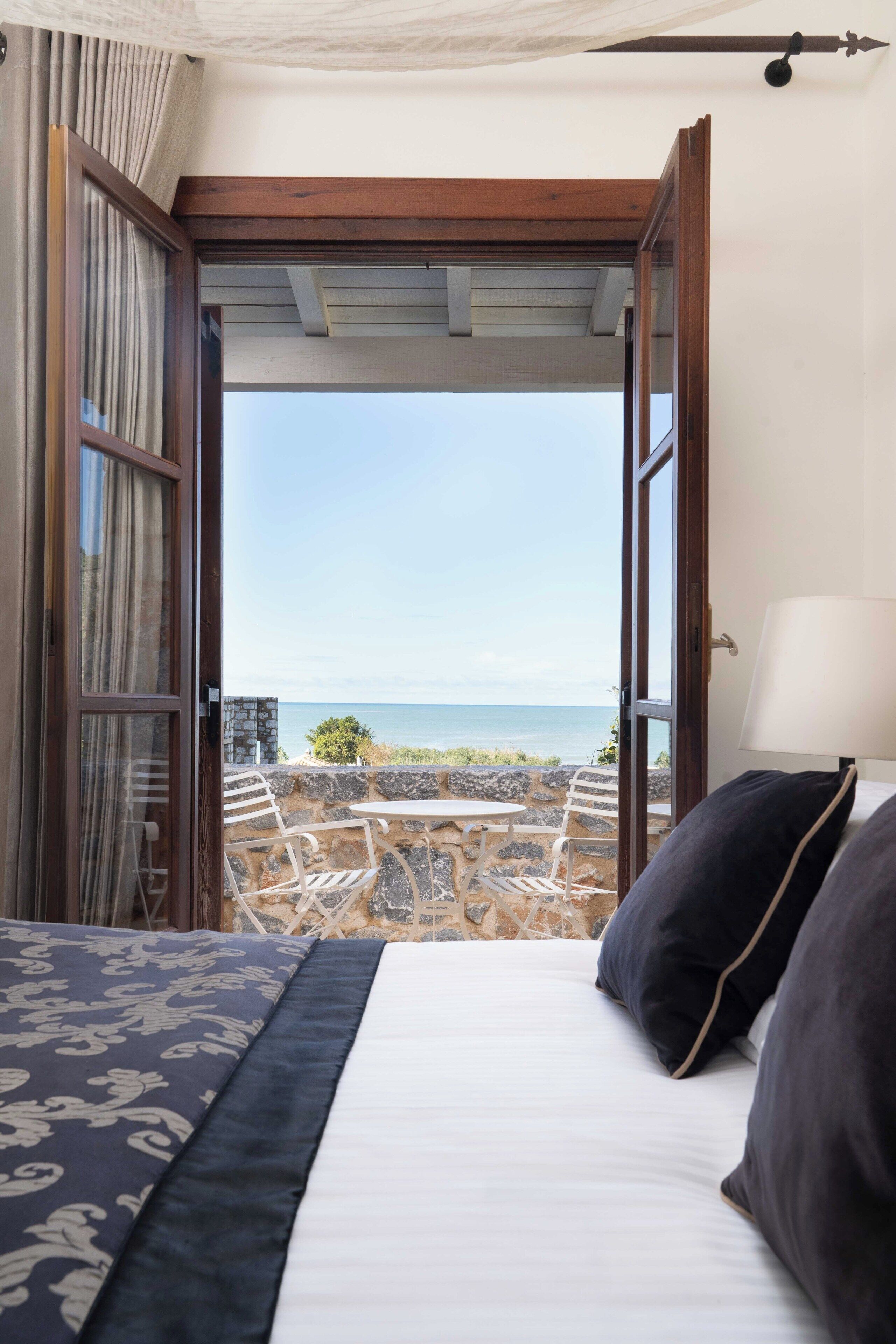 Un dormitorio con cama, vistas al mar y un patio con sillas y una mesa.