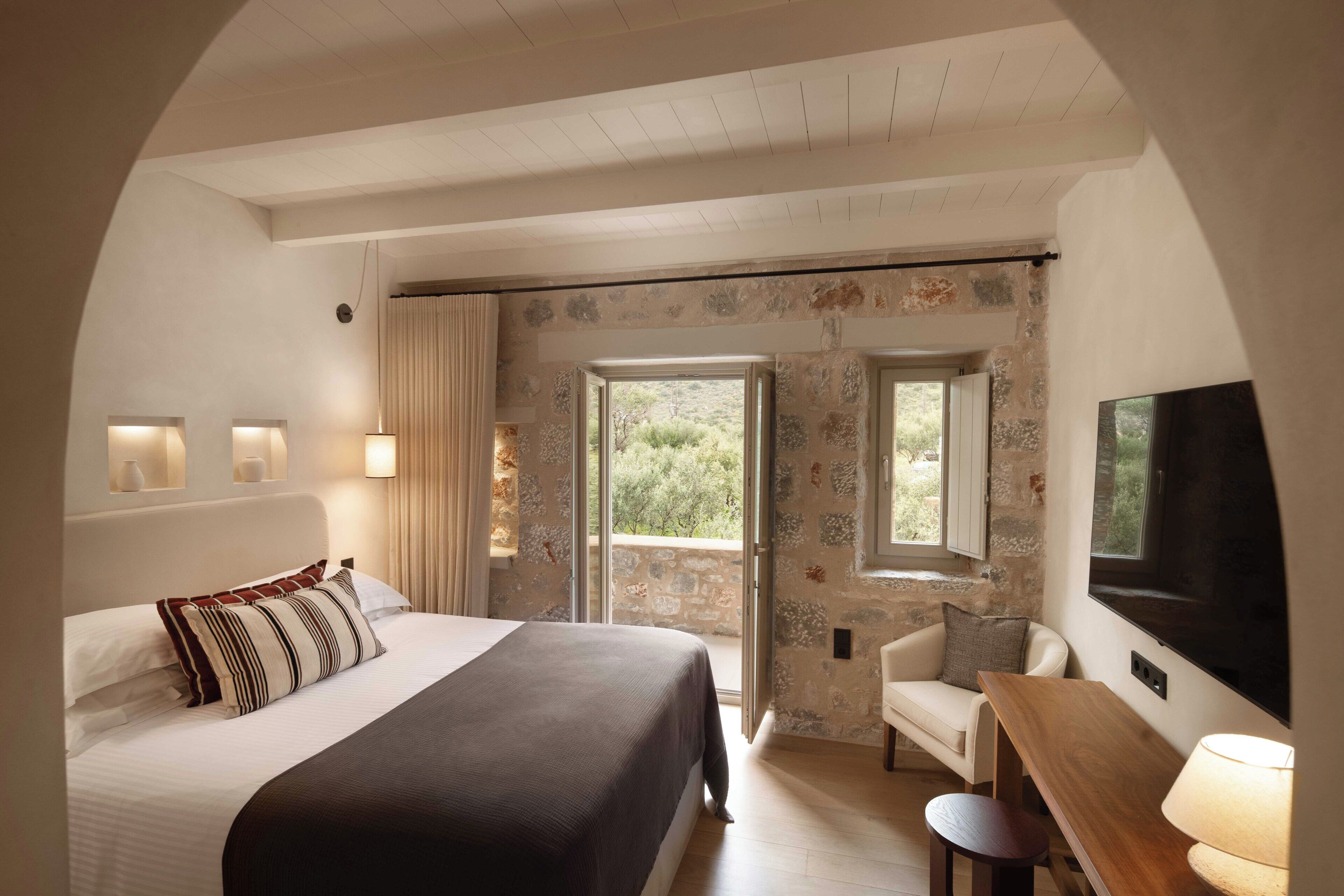 A bedroom with a bed, a desk, a chair, a TV, and a balcony with a view.
