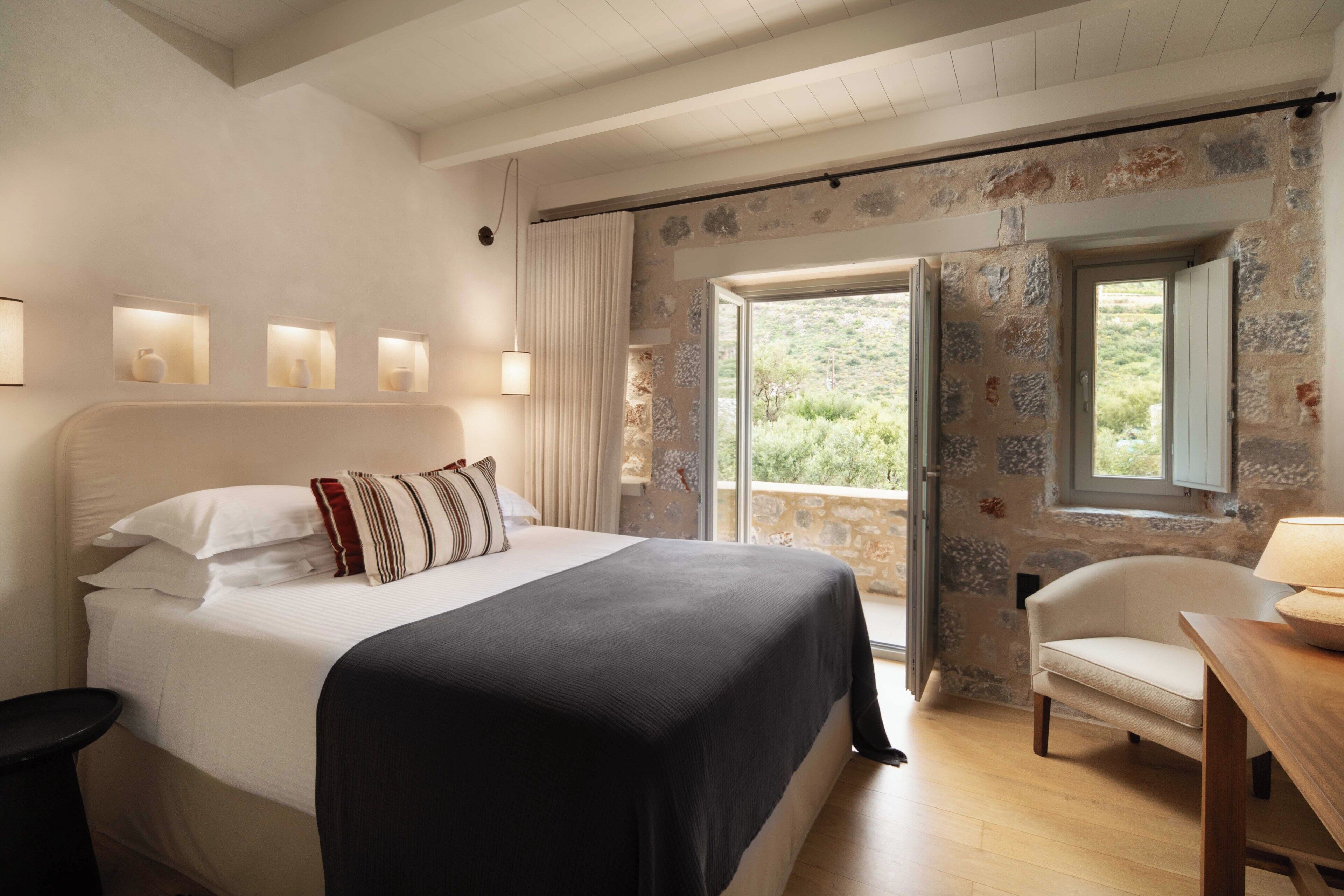 A bedroom with a bed, bedside lamps, a chair, a table, and a view through a window.