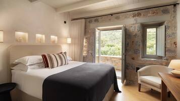 A bedroom with a bed, bedside lamps, a chair, a table, and a view through a window.