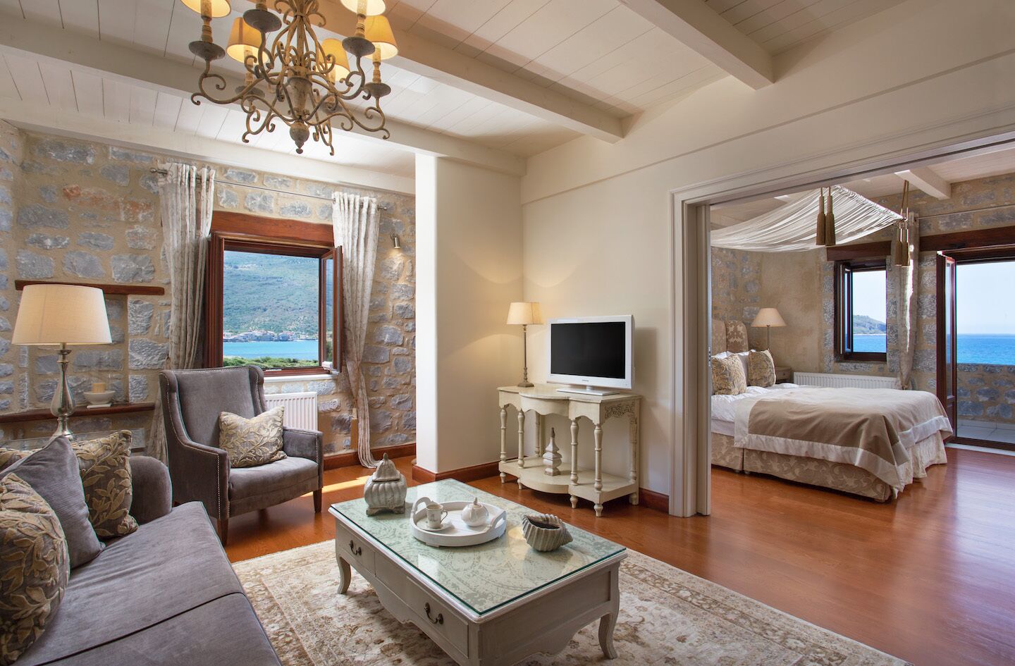 A room with a sofa, armchair, TV, and a bed with a view.