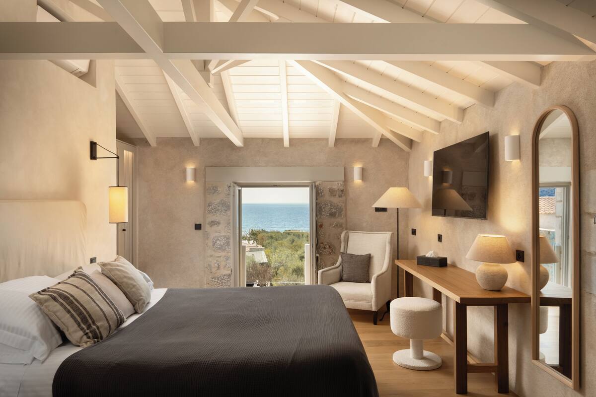Een slaapkamer met een groot bed, een bureau, een stoel en uitzicht op zee.