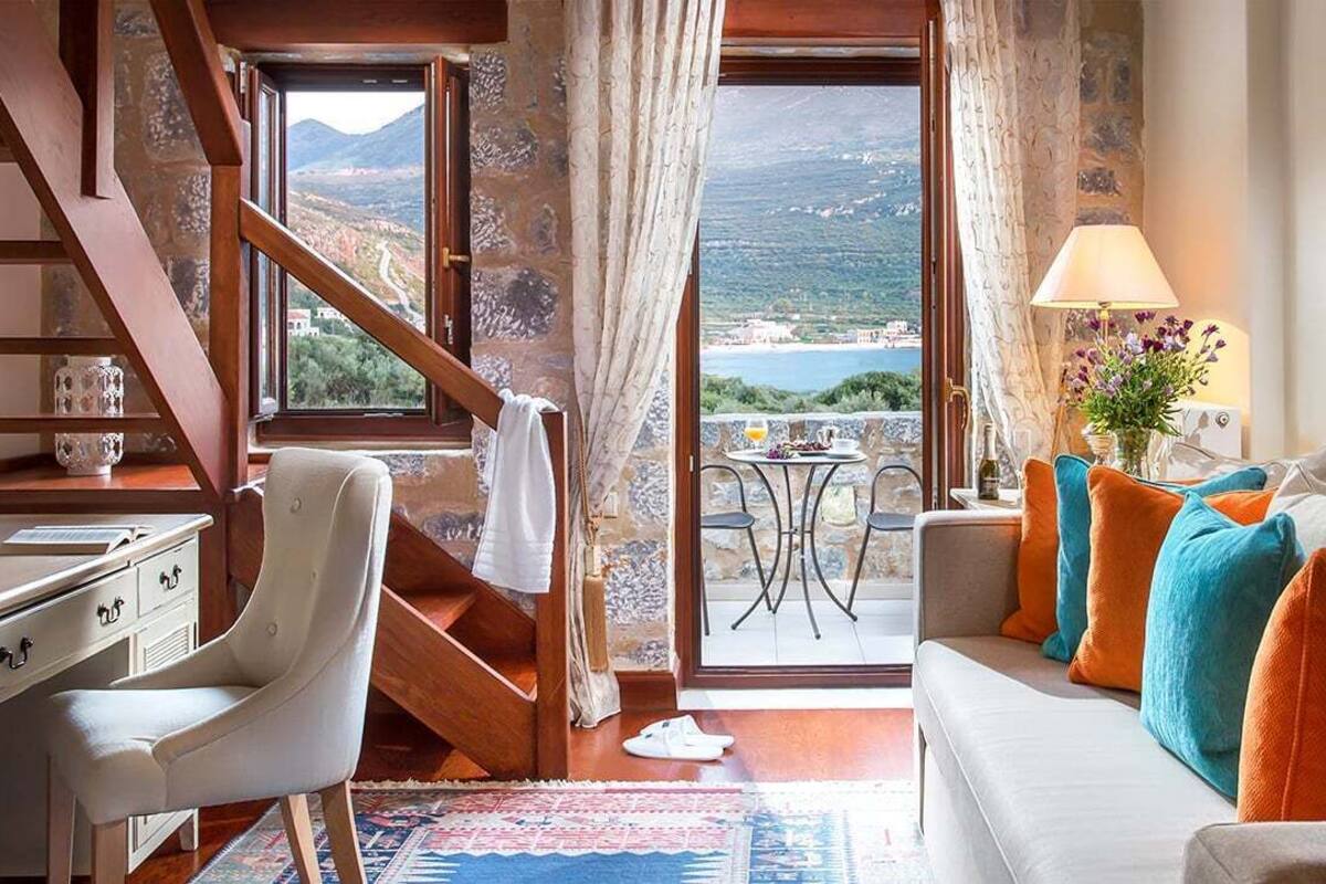 Een kamer met een bank, bureau, stoel, tafel, lamp en uitzicht op zee.