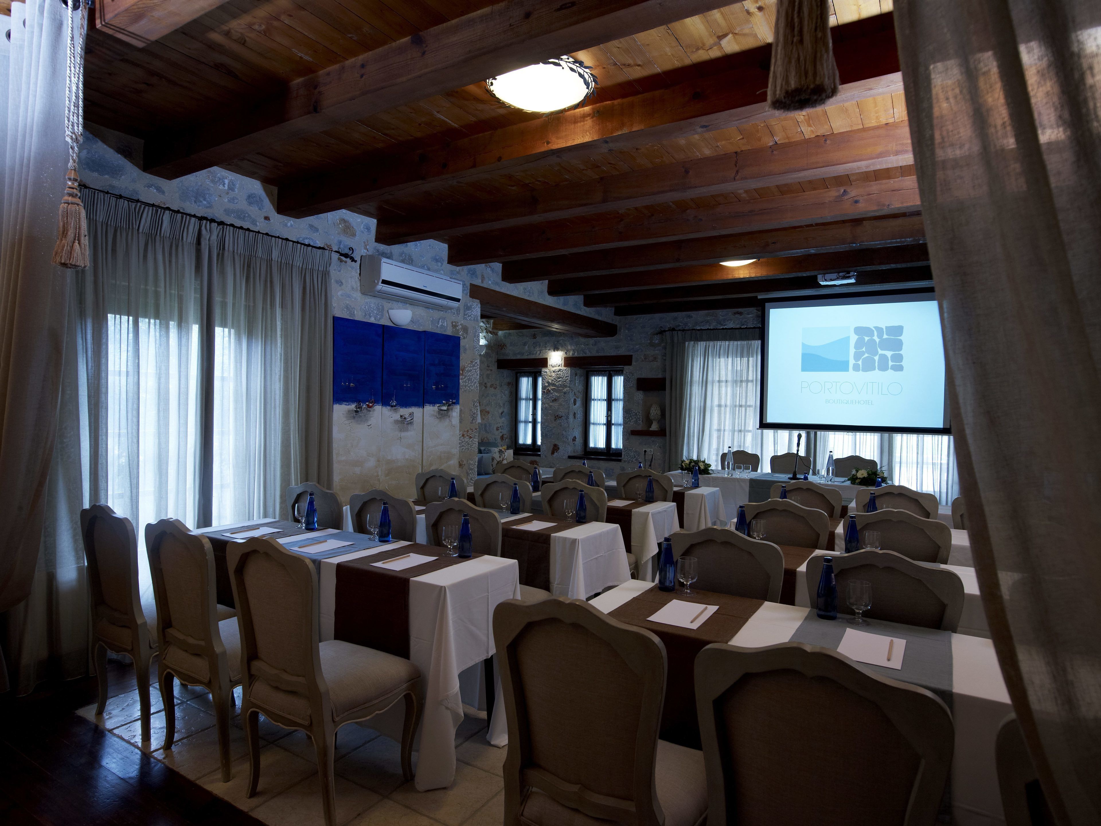 Un salón de conferencias con vigas de madera, mesas dispuestas para reuniones y una pantalla proyectando 