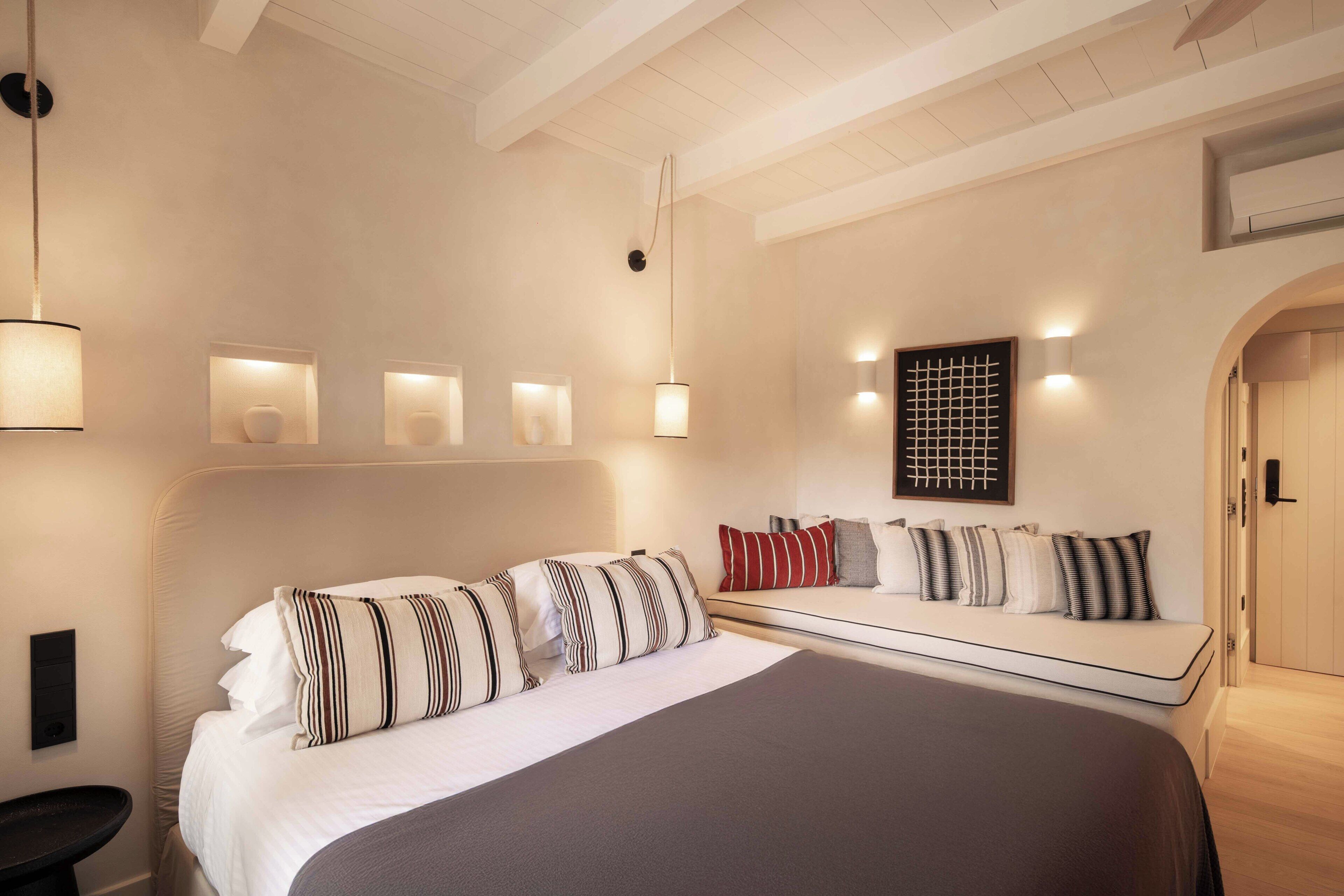 Een slaapkamer met een groot bed, nachtkastjes, een bank met kussens, wandlampen en een deur.