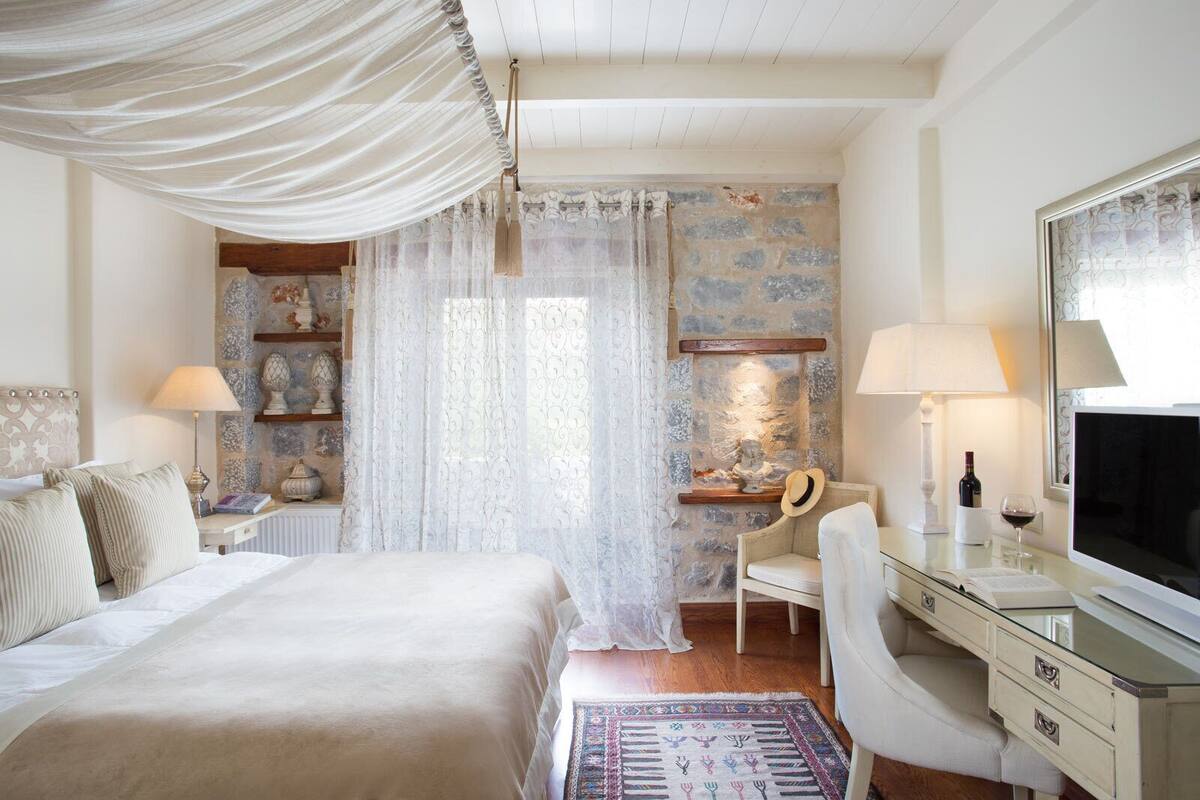 Een slaapkamer met een bed, een bureau, een stoel, een televisietoestel en een stenen muur.