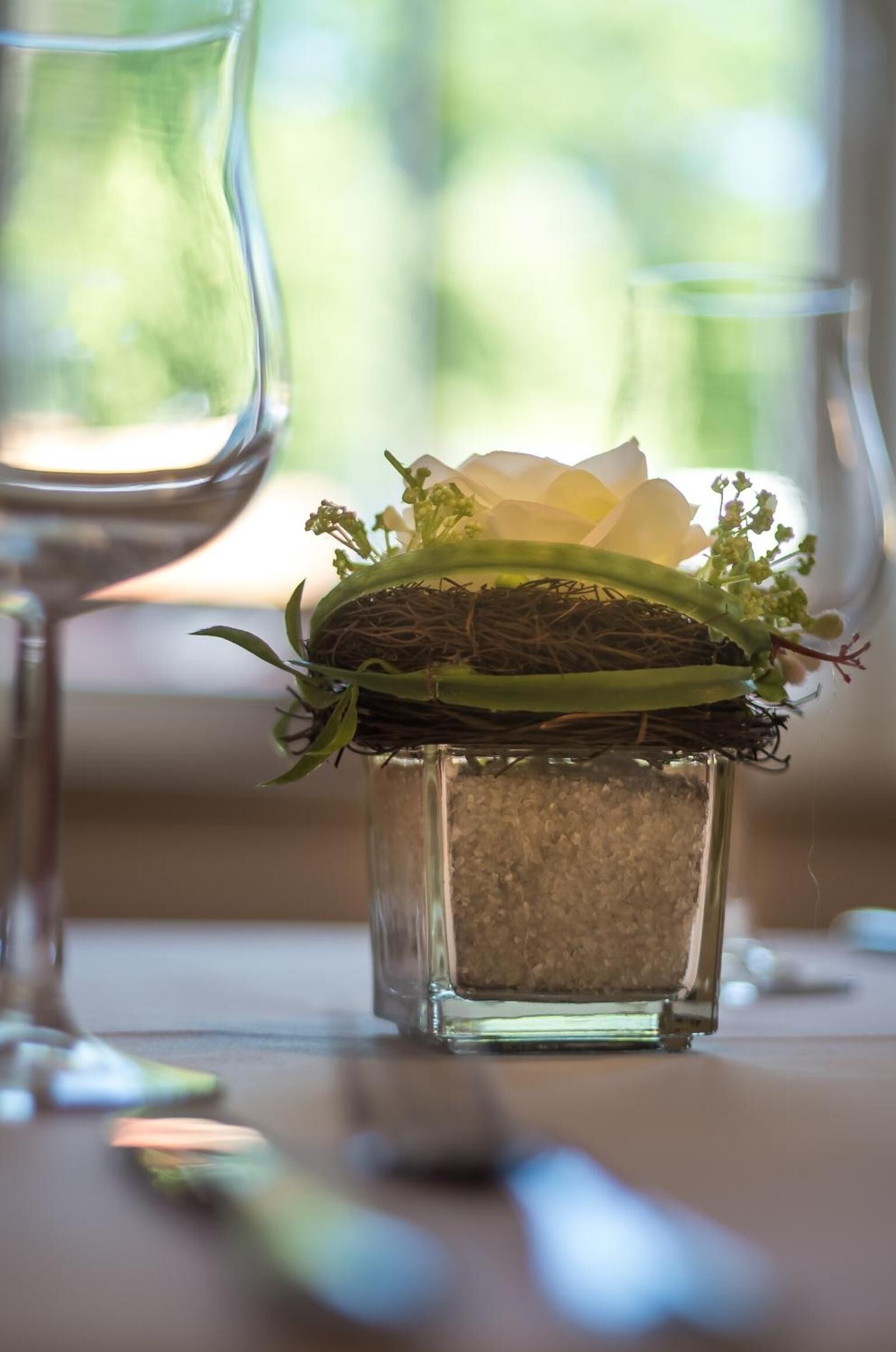 Ein gläserner Würfel mit einem Nest, grünen Blättern und weißen Blüten.