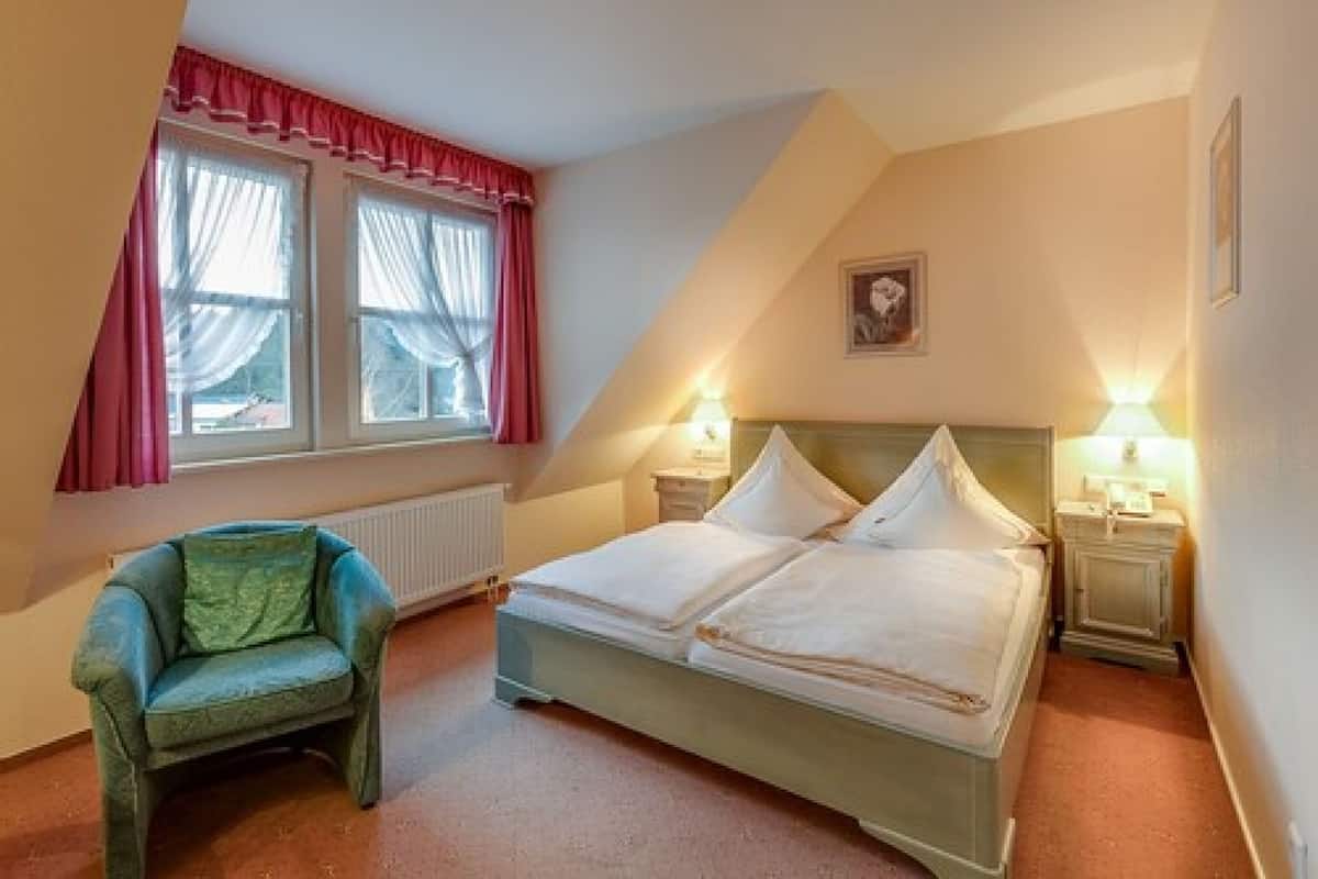 A bedroom with a bed, a chair, a window with curtains, and a picture on the wall.