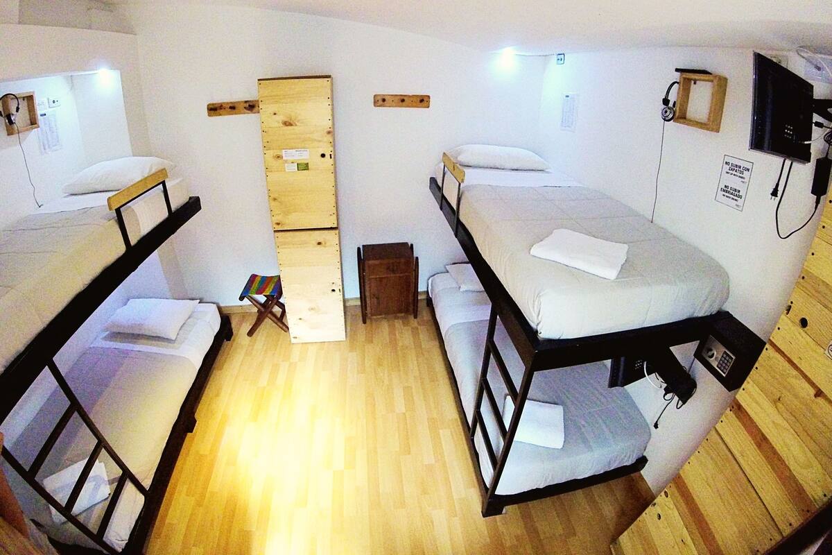 Una camera del dormitorio con letti a castello, uno sgabello, una porta in legno e una TV fissata al muro.