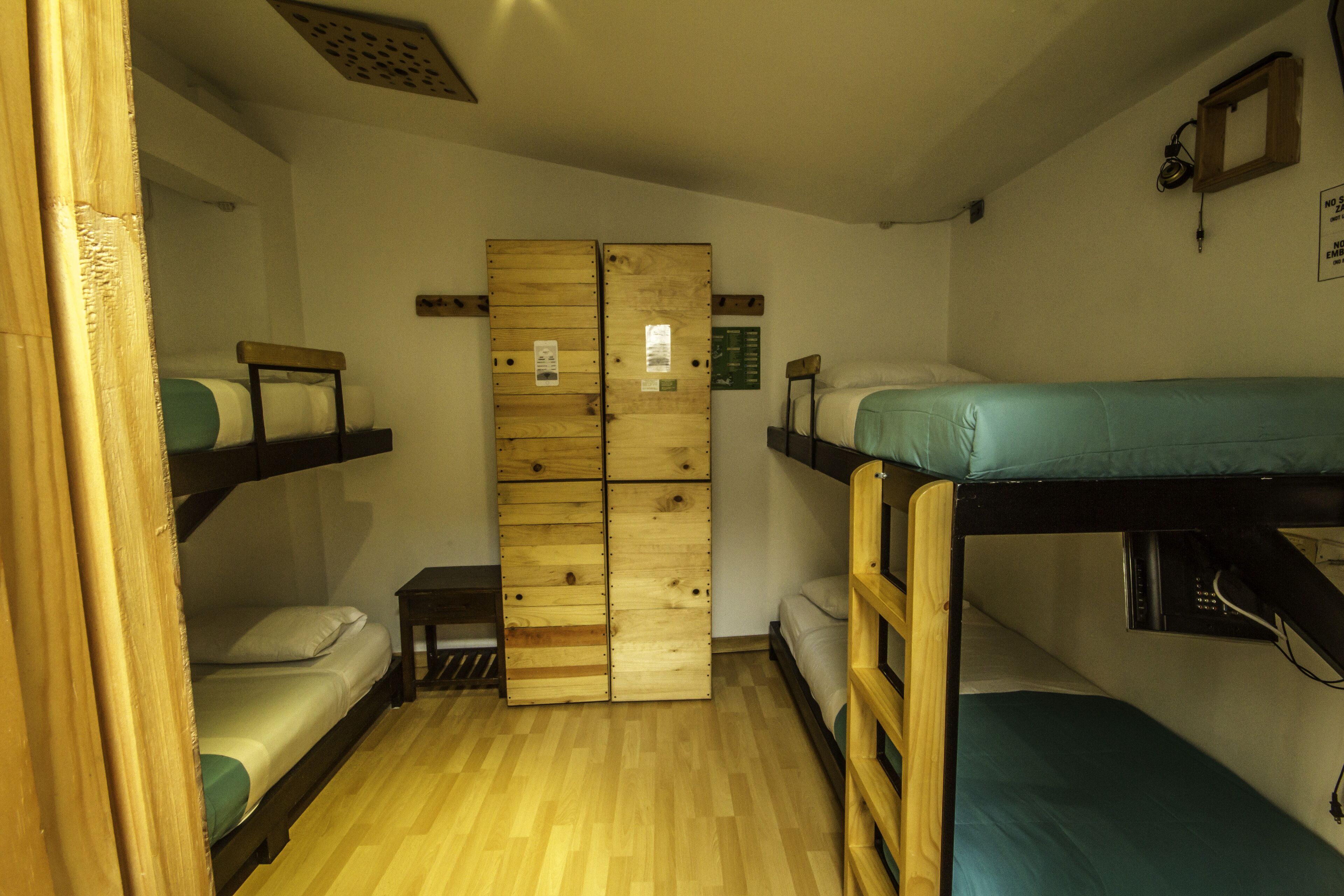 A dormitory room with bunk beds, a wooden wardrobe, and a small table.