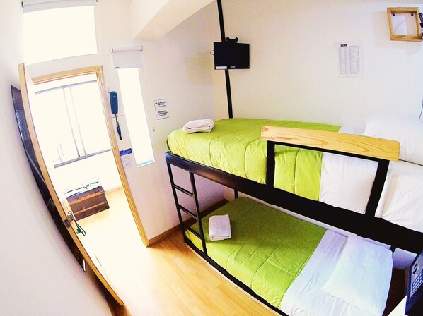 A bunk bed with a green mattress, a wooden headboard, and a white pillow. There is a black TV mounted on the wall and a door with a sign. - Hostal De La 57 - Hostel (Manizales)