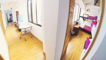 A room with a wooden floor, a white desk, a chair, a window, and a bunk bed with a pink bedspread.
