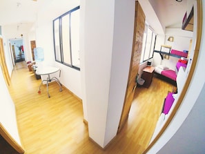 A room with a wooden floor, a white desk, a chair, a window, and a bunk bed with a pink bedspread. - Hostal De La 57 - Hostel (Manizales)