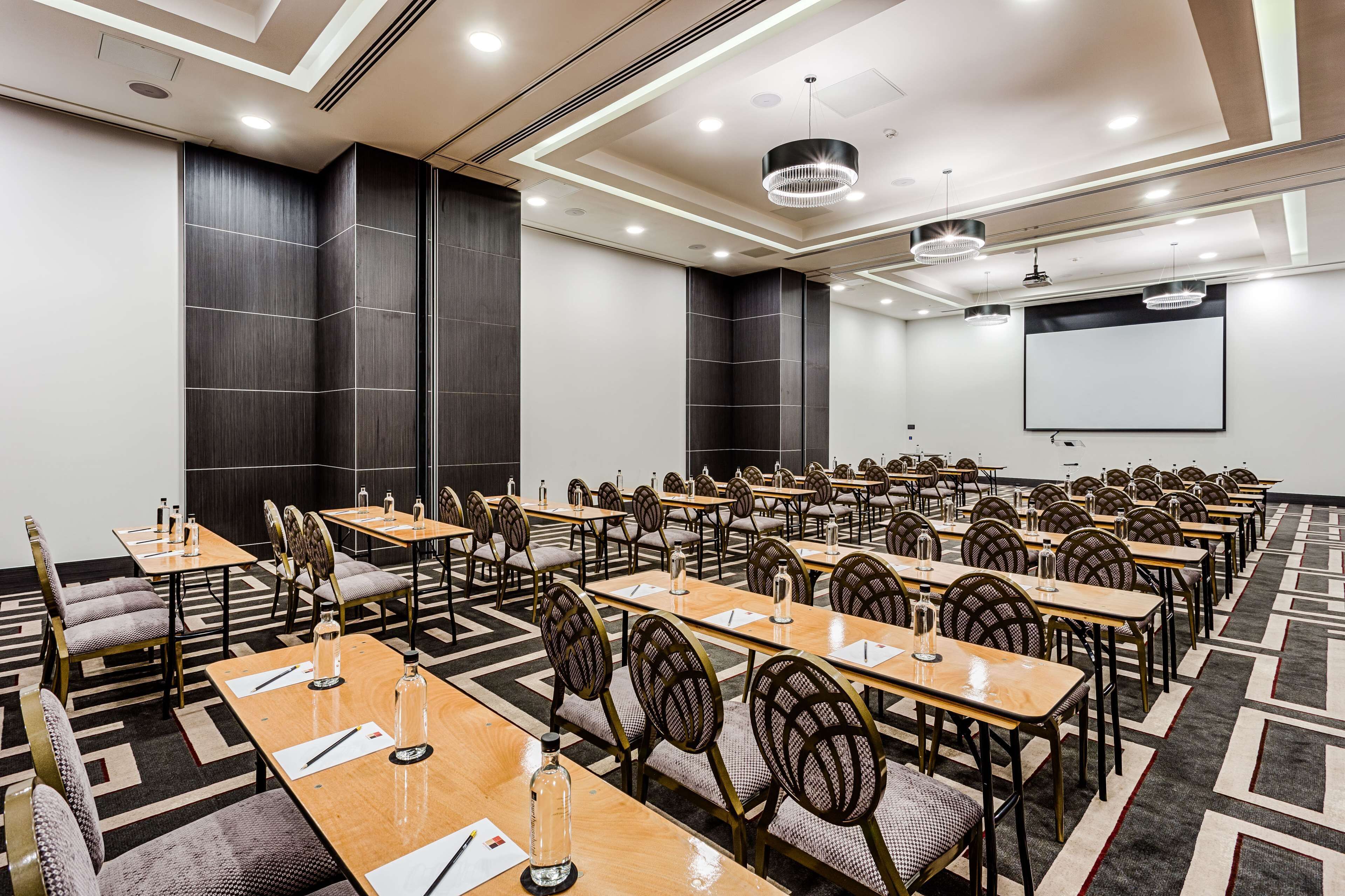 Una sala de conferències amb diverses taules, cadieres i una pantalla projectora.