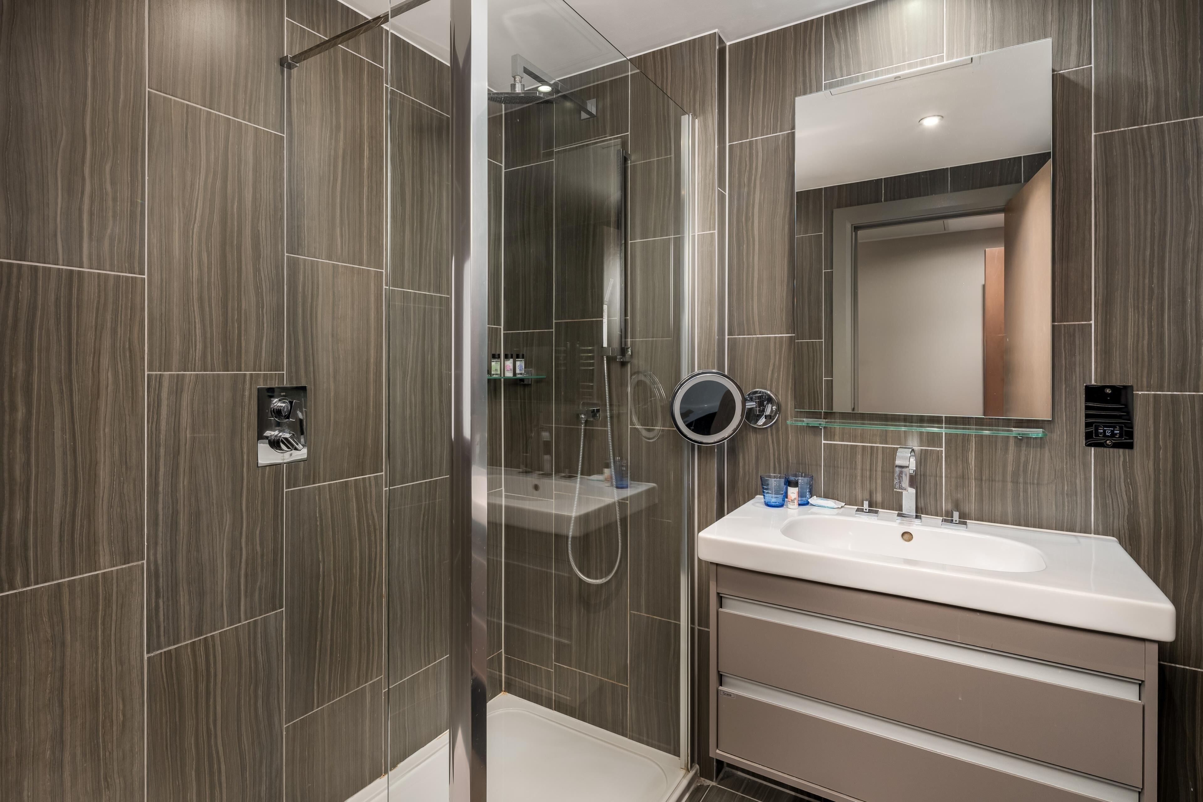 A modern bathroom with a glass-enclosed shower, a vanity with a mirror, and a sink.