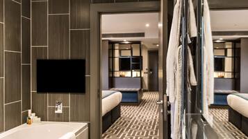 Une salle de bain d’hôtel moderne, dotée d’une grande baignoire, d’un téléviseur à écran plat fixé au mur et d’un carrelage décoratif.