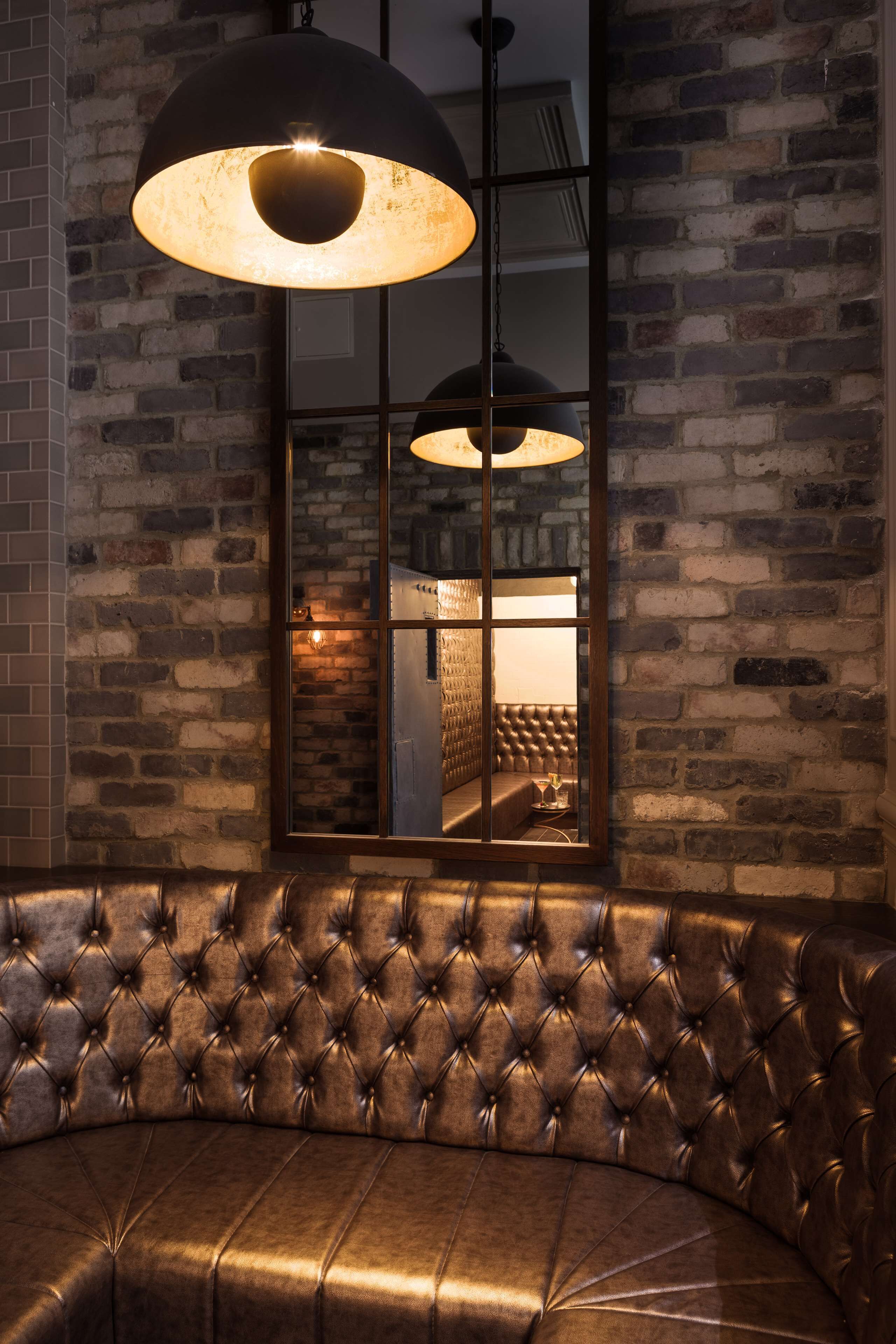 A leather sofa with a tufted design, a brick wall, and a large window with a view of a room.