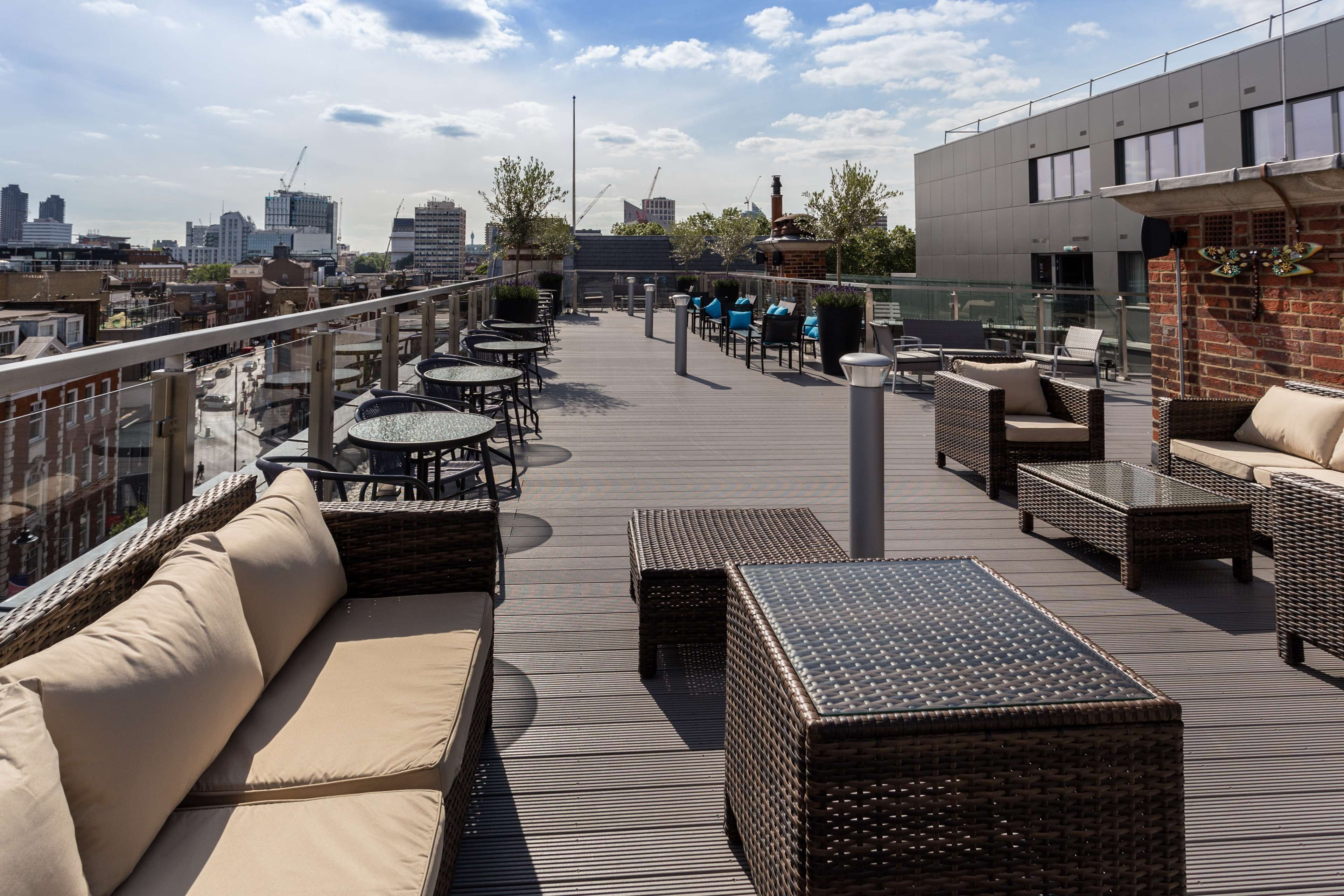En tagterrasse med udendørs siddepladser, udsigt over byen og en moderne bygning i baggrunden.