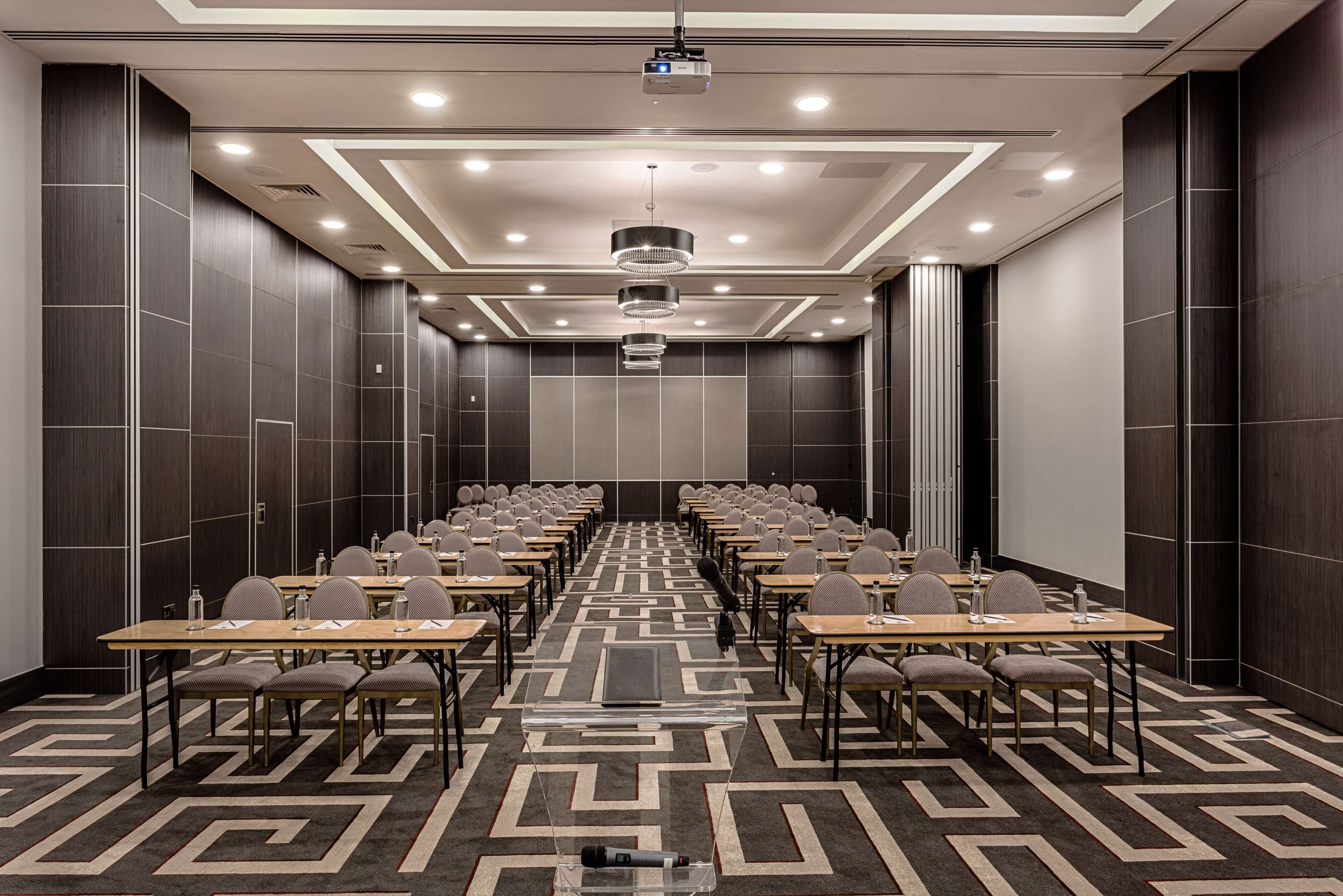 A conference room with rows of tables, chairs, a projector, and a microphone stand.