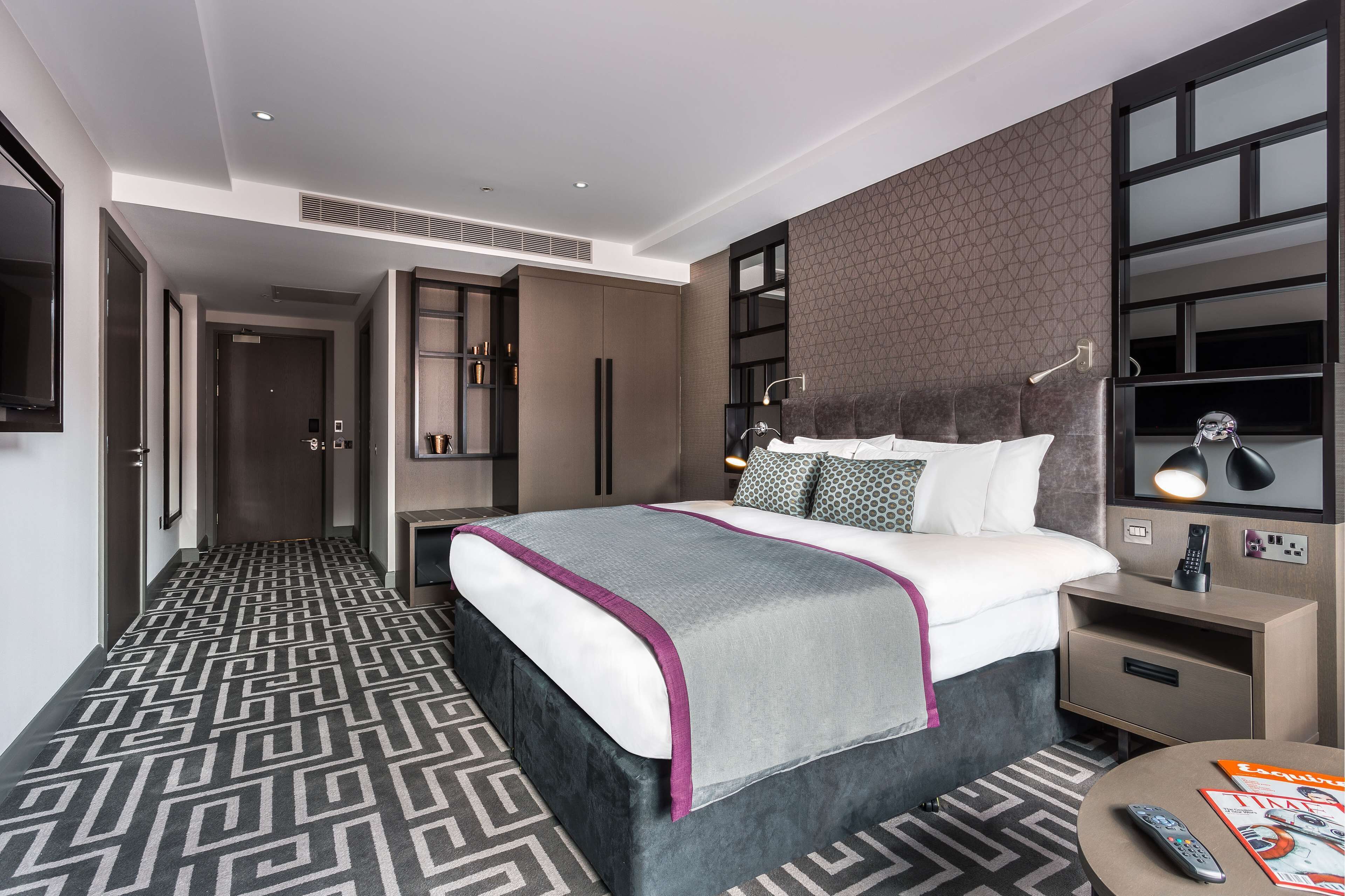 Een moderne hotelkamer met een groot bed, nachtkastje, televisie en een kamer met een patroon vloer.