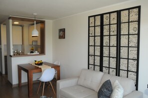 Una sala de estar moderna con un sofá, una mesa de comedor con sillas, una zona de cocina y un panel decorativo con firmas.