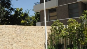Un immeuble moderne à plusieurs étages, doté de balcons, d’un mur de soutènement en pierre et d’un espace verdoyant bien entretenu, agrémenté de plantes.