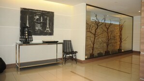 Un hall d’entrée moderne avec une cloison en verre, un fauteuil noir, une console en métal et un plan architectural encadré accroché au mur.