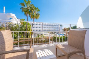 A balcony with wicker chairs and a white table, overlooking a pool and a white building with multiple balconies. - Hotel Antares (Santanyi)